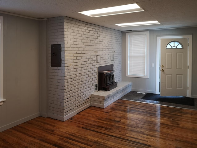 entrance foyer featuring a wood stove, brick wall, a drop ceiling, and dark wood-style flooring