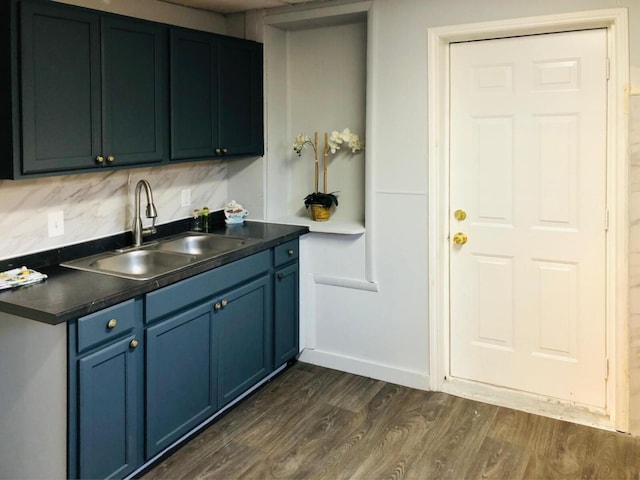 kitchen with tasteful backsplash, dark countertops, dark wood-type flooring, blue cabinets, and a sink