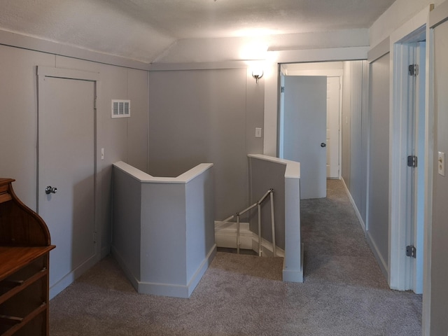 hall featuring carpet floors, visible vents, vaulted ceiling, and an upstairs landing