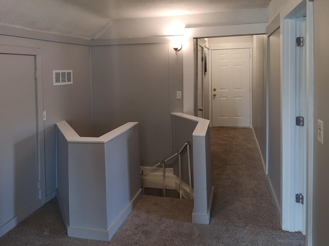 hallway with lofted ceiling, visible vents, dark carpet, and an upstairs landing