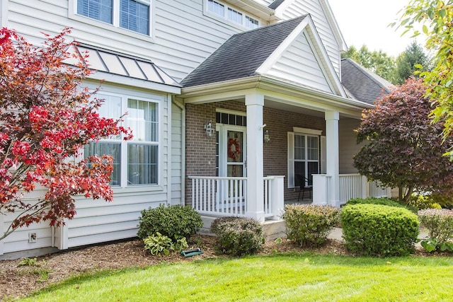 doorway to property with metal roof, roof with shingles, a standing seam roof, a porch, and brick siding