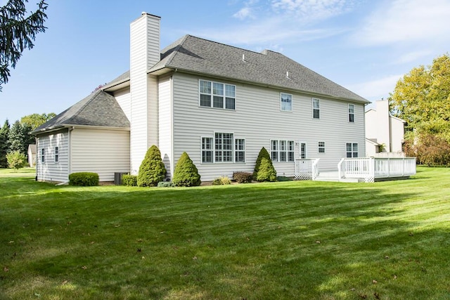 rear view of property featuring a chimney, a deck, a lawn, and roof with shingles