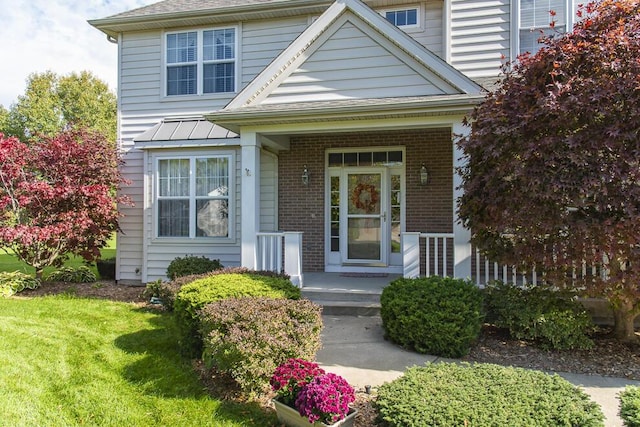 entrance to property with a yard, brick siding, and a porch