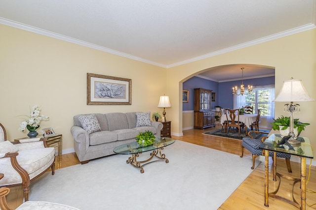 living room featuring arched walkways, a notable chandelier, ornamental molding, wood finished floors, and baseboards