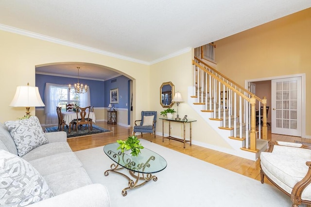 living area featuring arched walkways, stairway, wood finished floors, crown molding, and a chandelier