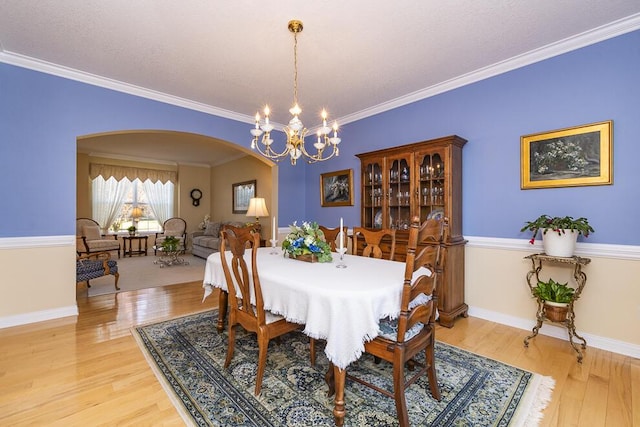 dining room featuring arched walkways, a chandelier, light wood-style flooring, baseboards, and ornamental molding