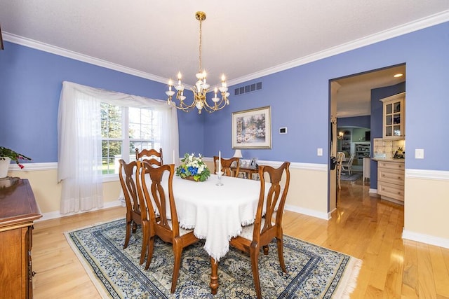 dining area with crown molding, visible vents, light wood-style floors, a chandelier, and baseboards