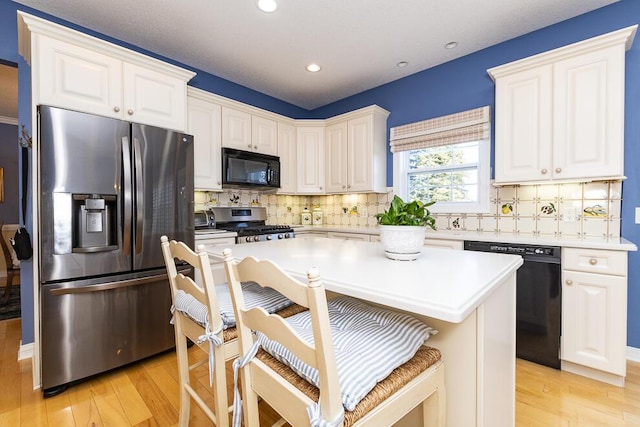 kitchen with a kitchen breakfast bar, white cabinets, light wood-style flooring, and black appliances