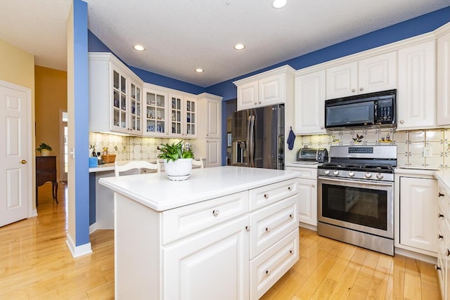 kitchen featuring light countertops, stainless steel gas stove, fridge with ice dispenser, light wood-type flooring, and black microwave