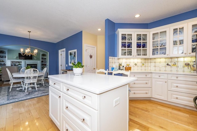 kitchen featuring tasteful backsplash, a kitchen island, light countertops, light wood-style floors, and a chandelier