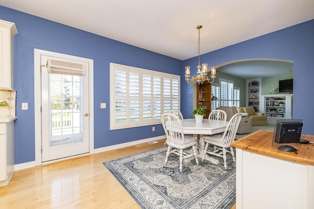 dining space featuring baseboards, light wood finished floors, arched walkways, and a notable chandelier