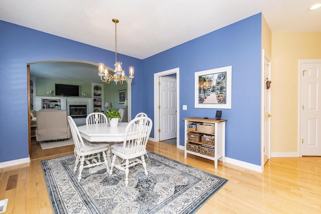 dining area with a chandelier, a glass covered fireplace, baseboards, and light wood finished floors