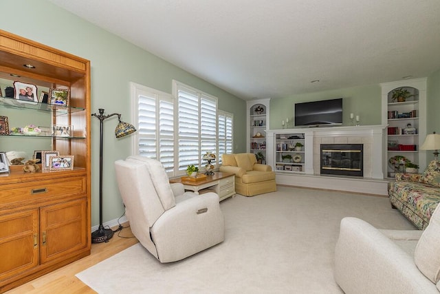 living room featuring built in shelves, a tile fireplace, and light wood-style flooring