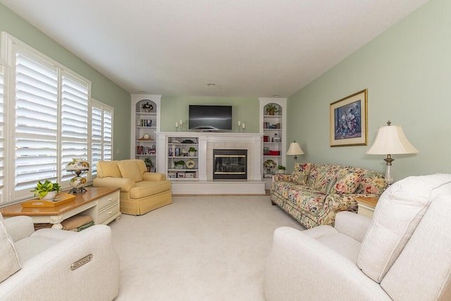 living room with built in shelves, carpet flooring, and a tiled fireplace