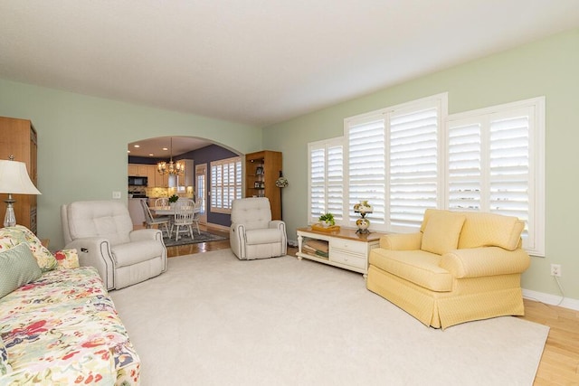 living room with arched walkways, light wood finished floors, baseboards, and a notable chandelier