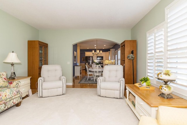 living area featuring light carpet, arched walkways, and a chandelier