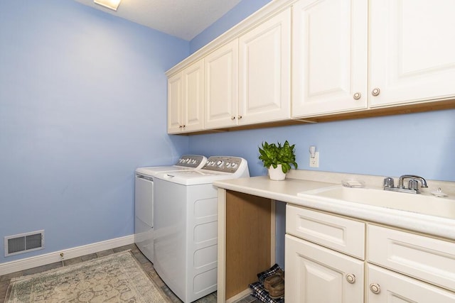 washroom featuring washing machine and dryer, a sink, visible vents, baseboards, and cabinet space