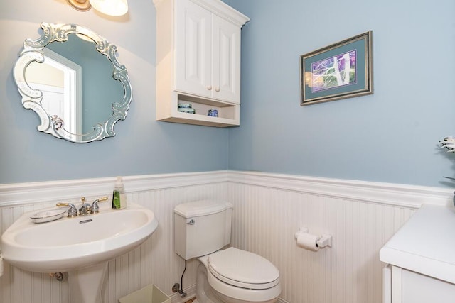 half bath with a wainscoted wall, a sink, and toilet