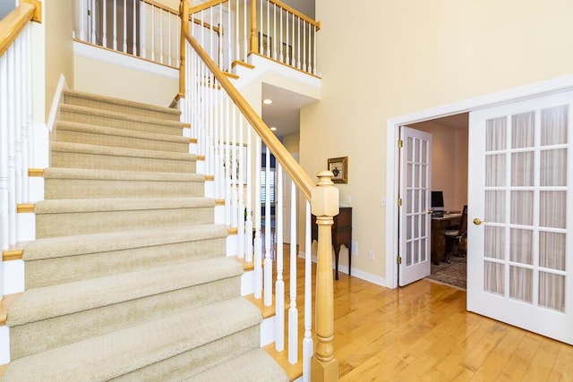 staircase with french doors, a towering ceiling, baseboards, and wood finished floors