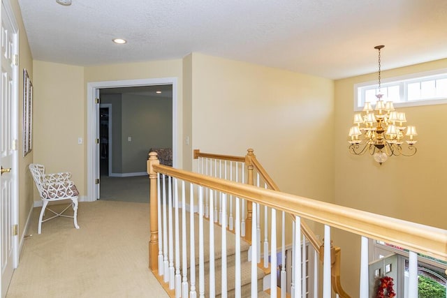 corridor with a textured ceiling, a notable chandelier, light colored carpet, an upstairs landing, and baseboards