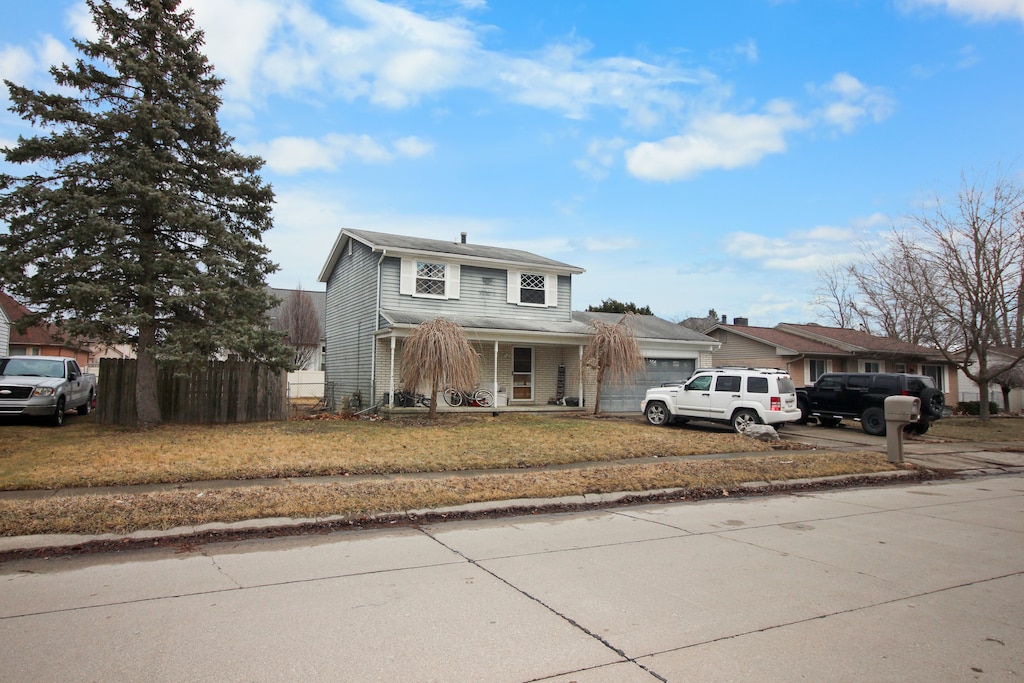 traditional-style house with driveway, an attached garage, fence, and a front lawn