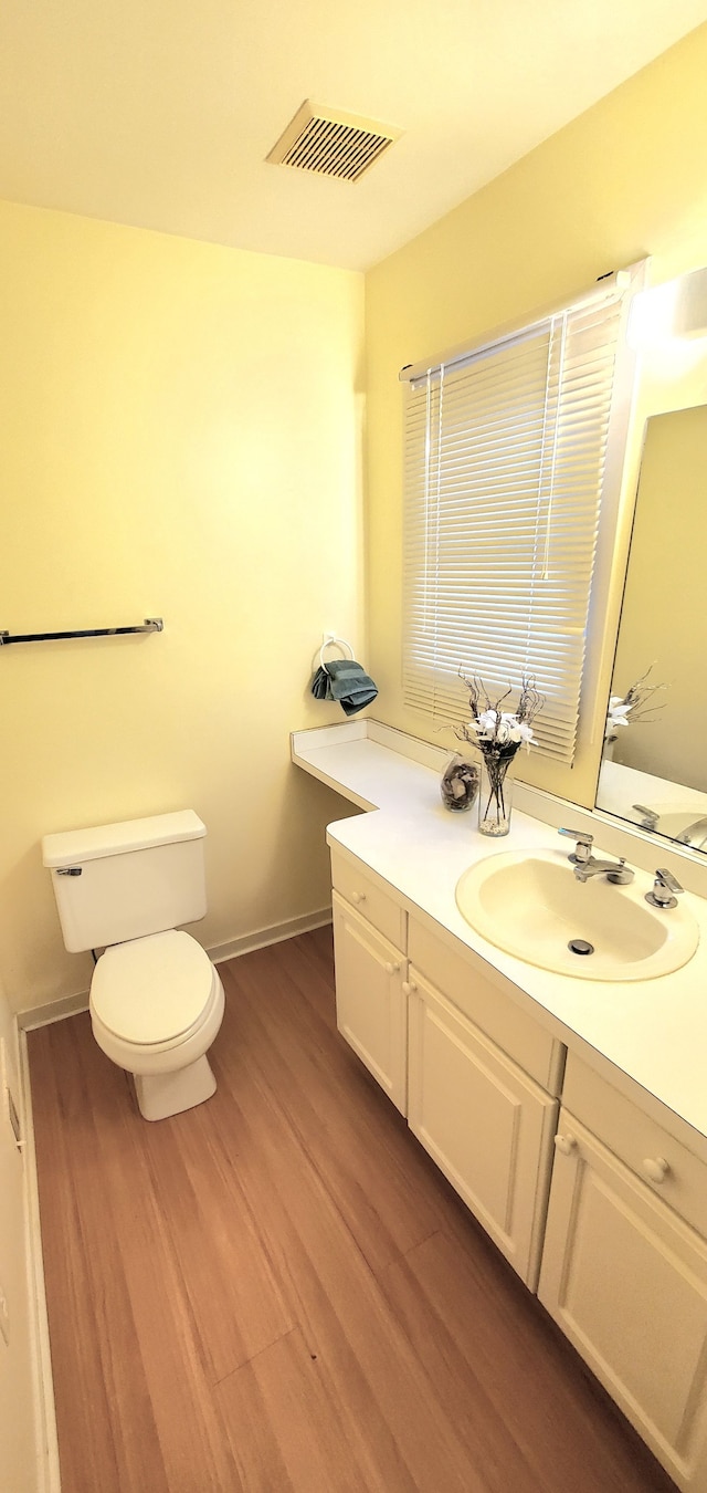 half bathroom with visible vents, baseboards, toilet, wood finished floors, and vanity