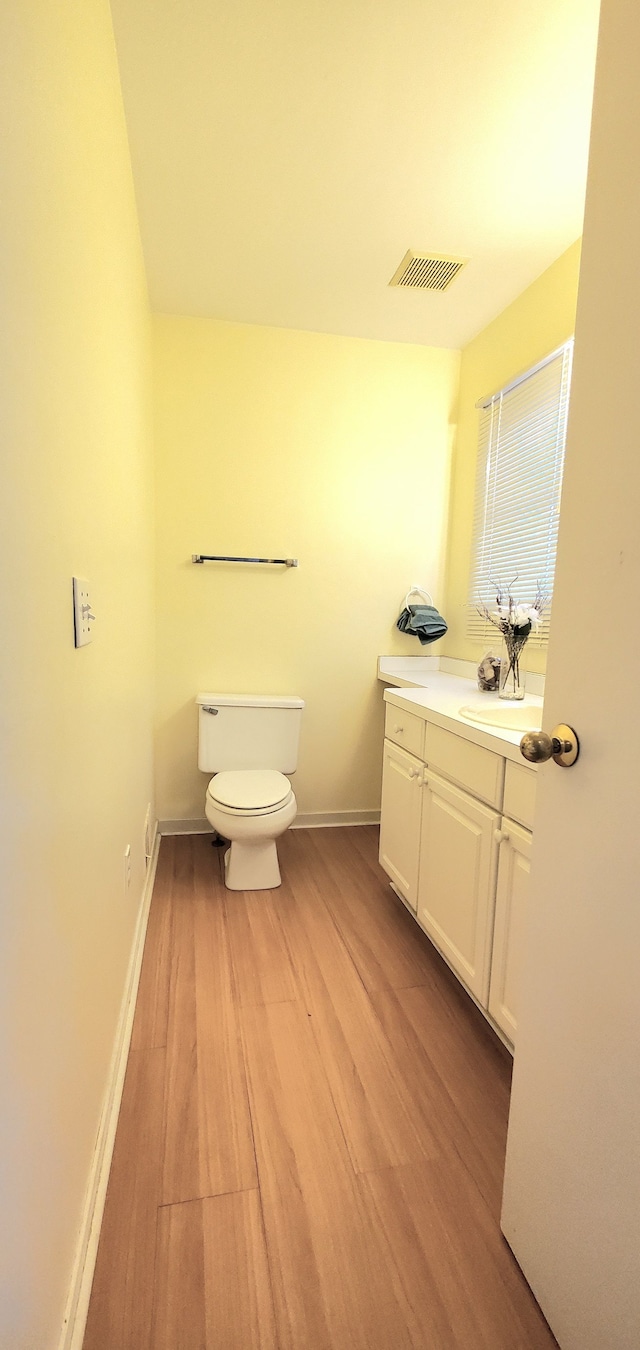 half bath with visible vents, baseboards, toilet, wood finished floors, and vanity