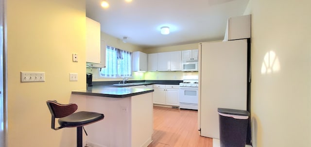 kitchen featuring a breakfast bar, dark countertops, white appliances, a peninsula, and white cabinets