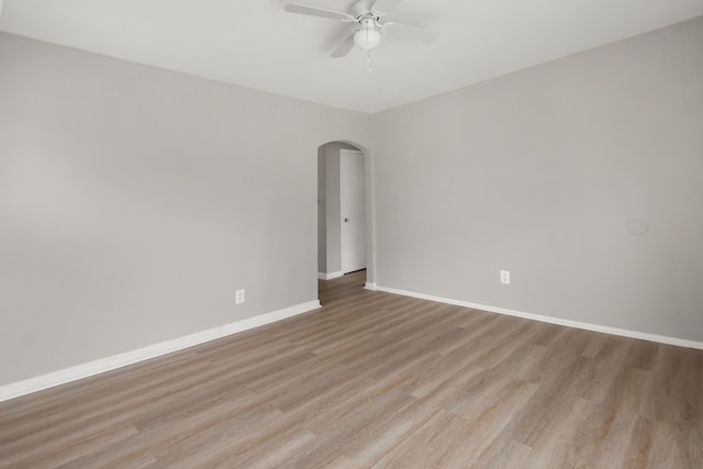 empty room with a ceiling fan, light wood-style flooring, arched walkways, and baseboards