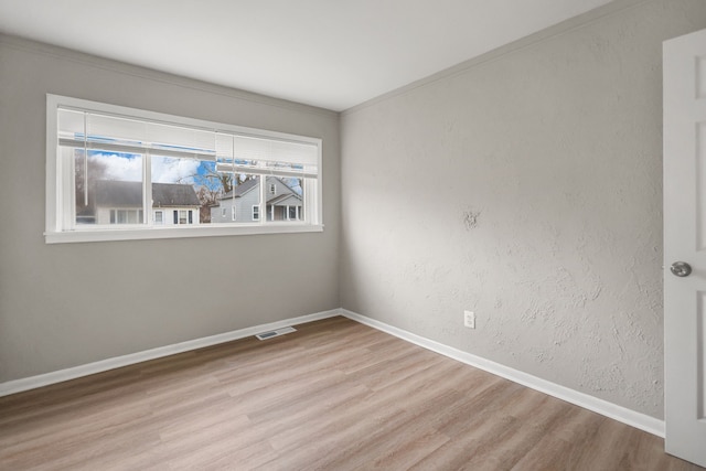 spare room featuring a textured wall, wood finished floors, visible vents, and baseboards