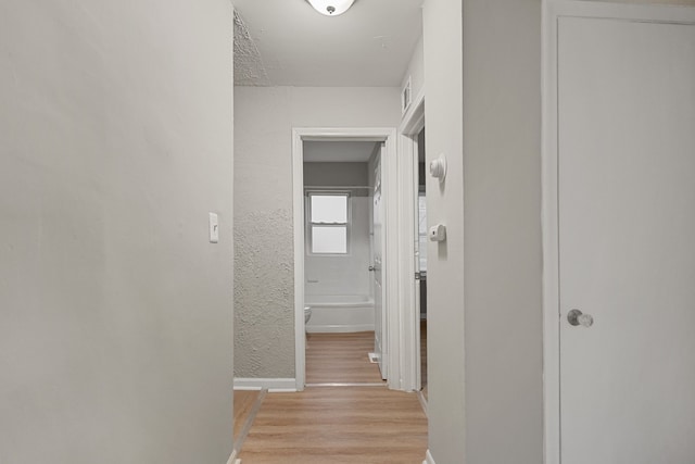 corridor featuring visible vents, a textured wall, light wood-style flooring, and baseboards