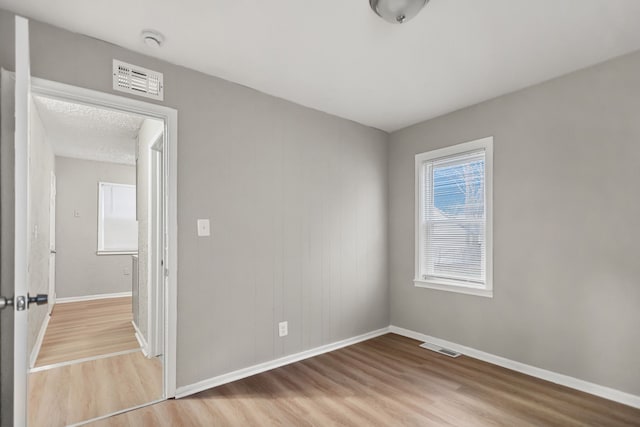 spare room with wood finished floors, visible vents, and baseboards