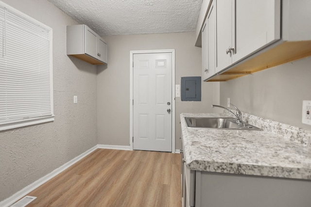 kitchen featuring electric panel, visible vents, light countertops, light wood-type flooring, and a sink