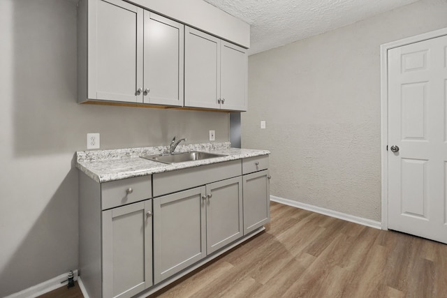 kitchen with a textured ceiling, light wood-style flooring, gray cabinetry, a sink, and baseboards