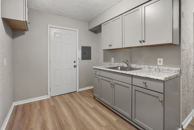 kitchen featuring a textured ceiling, gray cabinetry, a sink, light wood-style floors, and electric panel