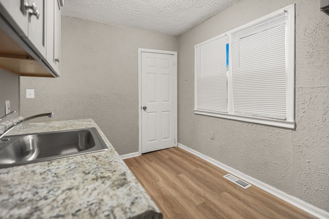 kitchen with a textured wall, light wood finished floors, a sink, and visible vents