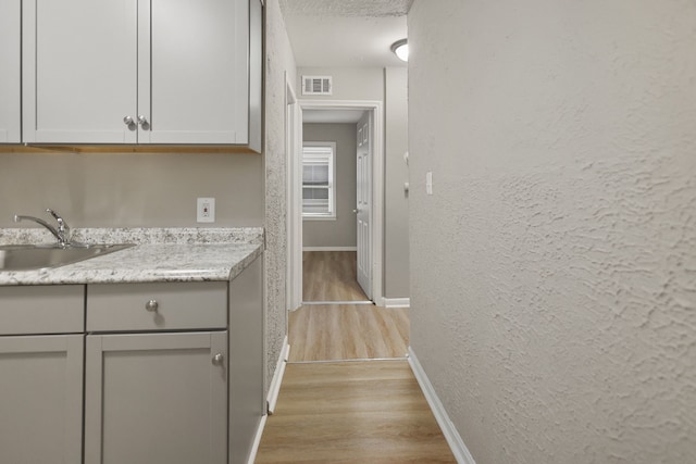 kitchen featuring baseboards, visible vents, a textured wall, light wood-style floors, and a sink