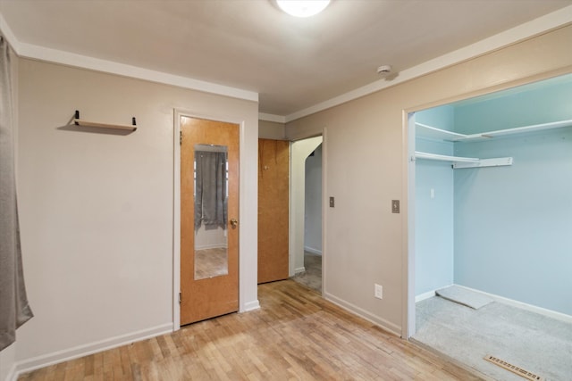 unfurnished bedroom with crown molding, a closet, wood finished floors, and baseboards