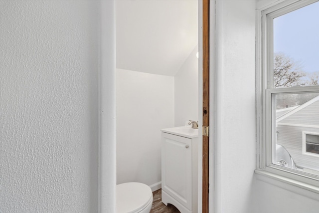 half bathroom with a textured wall, vanity, and toilet