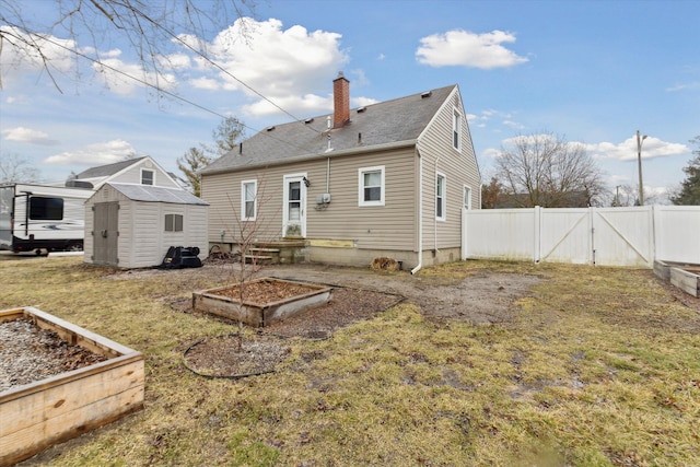 rear view of property featuring an outbuilding, a vegetable garden, a chimney, a storage unit, and fence