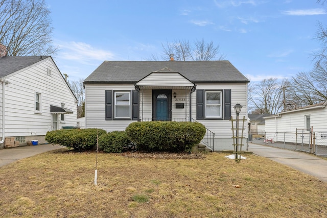 bungalow-style home featuring concrete driveway, roof with shingles, a gate, fence, and a front lawn