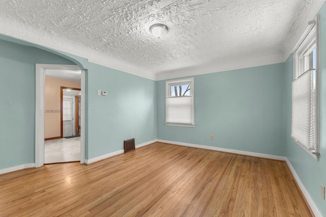 empty room with arched walkways, visible vents, light wood-style flooring, and baseboards