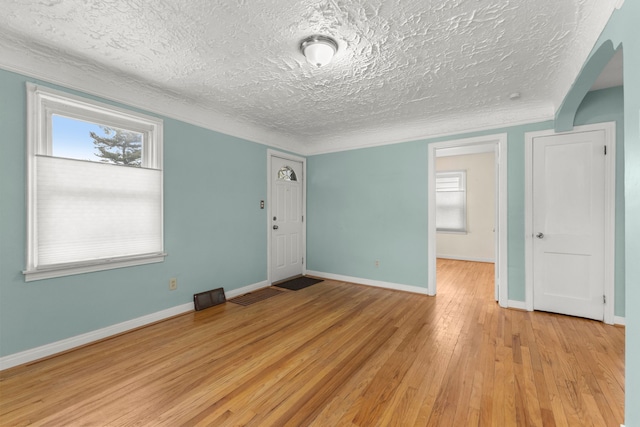 spare room with a textured ceiling, visible vents, baseboards, light wood-style floors, and ornamental molding