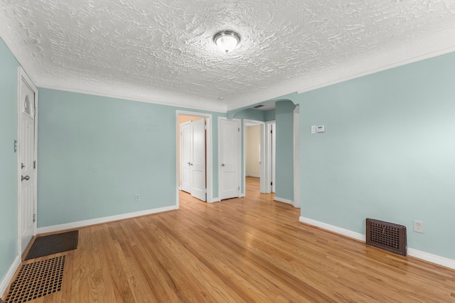 unfurnished room featuring arched walkways, light wood finished floors, visible vents, and baseboards