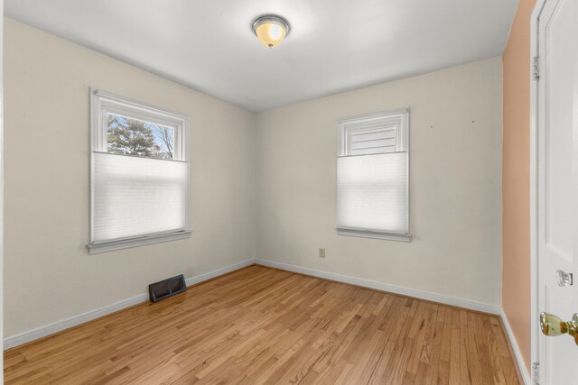 empty room with light wood finished floors, visible vents, and baseboards