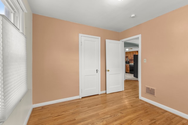 unfurnished bedroom featuring freestanding refrigerator, light wood finished floors, visible vents, and baseboards