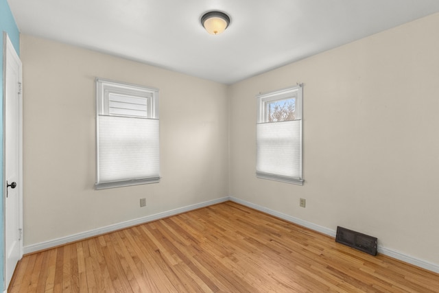 spare room with light wood-type flooring, visible vents, and baseboards