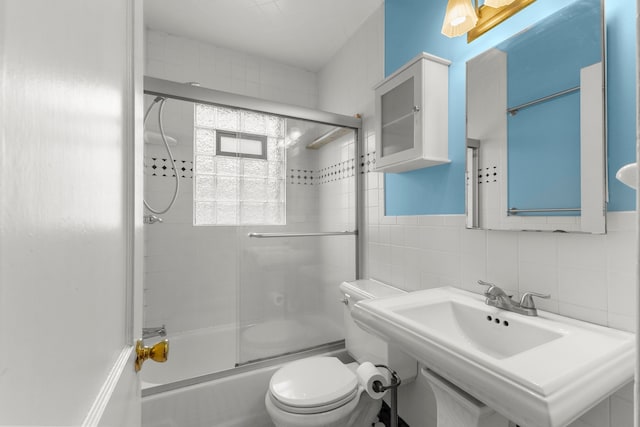 bathroom with toilet, combined bath / shower with glass door, a sink, and tile walls