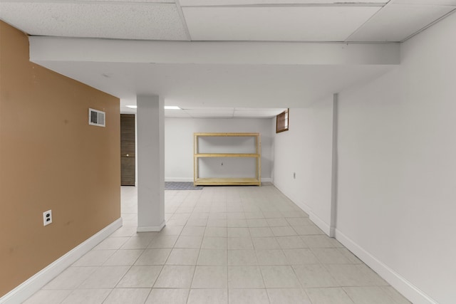 finished basement featuring light tile patterned floors, a paneled ceiling, visible vents, and baseboards