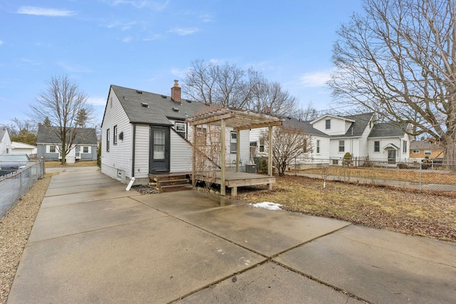 rear view of property with fence, driveway, a wooden deck, a pergola, and a chimney